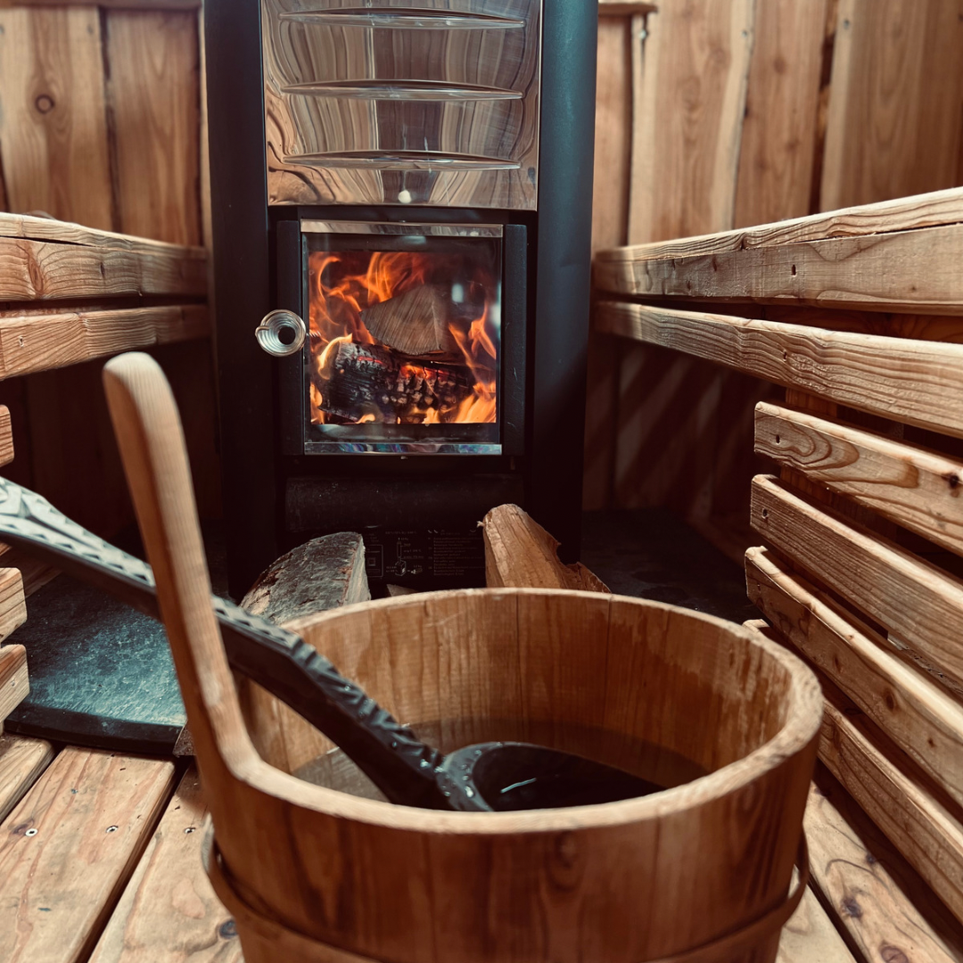 Brændefyret sauna med blus i ovnen og spand ved siden af